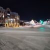 Ночная улица Ямала с яркими огнями на фоне современного здания, освещенная декорация и светящиеся дуги на тротуаре, атмосфера тундры и города