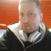 Уверенный взгляд человека в худи и серых наушниках на фоне оранжевых панелей и яркого света, в теме «ПРЕДЕЛ ЛЮБВИ» от Nordlove