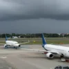 A realistic scene showing two regional airports in the southern part of a country under a stormy sky, with runway lights turned off, gates empty, and aircraft parked and covered, conveying the sense of flight disruptions; include distant cityscape and dark clouds, but no signage or textual elements
