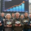 A diverse group of Russian adults standing in a bustling city square, each holding a visibly heavy wallet filled with bills, while a large digital billboard above them displays an upward trending salary graph, all captured in a realistic, detailed style