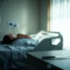 A somber, realistic scene showing a hospital room with a faint silhouette of a woman lying on a bed, a medical monitor displaying vital signs, and on a nearby table a stainless steel knife and a small glass bottle of acid placed apart, illuminated by soft, diffused light to convey seriousness without graphic detail