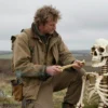 An archaeologist in a British field examining a Mesolithic child's skeletal remains, wearing field gear and holding a bone, with a small child skeleton in the foreground, set against a prehistoric landscape, no modern technology, no text