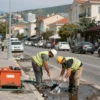 A bustling street in Sochi with workers cleaning stormwater drains, showing a clear view of the cityscape, with equipment and hoses, no text or signage