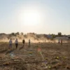 A sunny landscape of the Ulyanovsk region with heat waves rising from the ground, people wearing light clothing walking or standing in a field or cityscape, a bright sun overhead, no text or symbols in the image