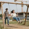 A realistic scene of a small-town playground with a wooden swing set, a young girl captured mid-air as she falls off the swing, a concerned adult watching nearby, and a construction crane and partially built structure in the background to indicate a contractor's presence, under a clear sky