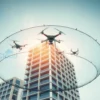 A modern urban building surrounded by a futuristic two-layer protective net, with small unmanned aerial vehicles (UAVs) approaching and being intercepted by the net; the scene shows the net's dual layers clearly, one outer mesh catching drones and an inner layer providing extra safety, under a clear sky; realistic lighting and perspective emphasize the technology and security aspect