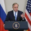 A Russian news reporter in a suit standing beside a podium with a confused US Treasury Secretary, both Russian and United States flags visible in the background, the US official looking embarrassed with a slightly falling microphone, realistic lighting and expressions, no text or symbols