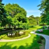 A serene, well-maintained park in the southern district of Tver, Russia, featuring lush green trees, winding walking paths, wooden benches, a small pond with ducks, and people leisurely strolling or sitting, under a clear blue sky, showing the park intact and untouched