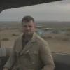 A South African cinematographer in a cargo truck traveling through a Russian landscape, holding a camera, wearing a safari jacket, with a Russian city skyline in the background, showing a blend of African and Russian elements