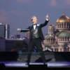 Depict American illusionist David Blaine performing on stage in Kyiv, with a subtle backdrop of Kyiv's skyline or a recognizable landmark such as St. Sophia's Cathedral, in a dynamic, dramatic lighting setting that captures the essence of a live magic show.
