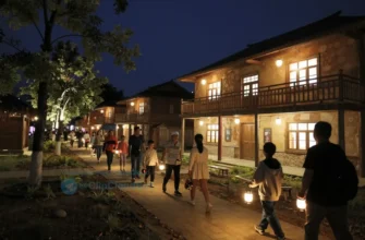 A nighttime village scene in Lopshen'ga where locals and visitors are engaged in a museum-themed quest. The image shows a small, rustic museum building illuminated by warm lights, with a group of people—children, adults, and elders—following a trail of glowing clues and lanterns. The village streets are lined with traditional wooden houses, and a few trees glow softly. The atmosphere is adventurous yet cozy, capturing the excitement of a community event turned into a quest.