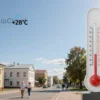 A bright, sunny street scene in Saransk on May 17, featuring a clear blue sky, a warm sun, and a typical Russian cityscape with modest buildings and trees. The temperature is depicted by a subtle, realistic thermometer icon showing +28°C, but no textual labels or numbers are included. The scene conveys a pleasant, warm atmosphere with people casually walking or standing outdoors, wearing light clothing.