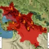 A detailed, realistic depiction of the Volgograd region map with high fire risk zones highlighted in red, surrounded by forested and agricultural landscapes, subtle flames rising from the highlighted areas, and a prominent warning sign in the corner, all rendered in a high-resolution horizontal format