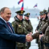 A dignified scene showing a male political leader resembling a Russian president in a formal suit, shaking hands and smiling while standing among a group of uniformed border guard officers in winter camouflage gear, with a snowy border checkpoint background and subtle flags waving, conveying a congratulatory atmosphere