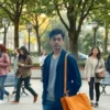 A thoughtful, realistic scene showing a diverse group of people in a public setting, with one individual subtly highlighted to represent hidden mental health struggles; the highlighted figure appears slightly translucent or surrounded by faint, abstract swirling patterns that suggest inner turmoil, while the surrounding people appear normal and unaware, conveying the concept that many suffer silently; the background is a city park with trees and benches, soft natural lighting, no text or symbols