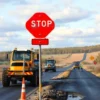 A construction crew repairing two damaged roads in the Yaroslavl region, featuring heavy machinery, road signs, and a scenic rural background that highlights progress and safety measures