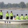 A group of security personnel in bright uniforms aboard patrol boats on a river, monitoring the water, with a scenic riverbank in the background, in a realistic style