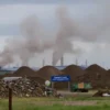 A realistic view of a large garbage landfill near the town of Novoshakhtinsk, with piles of waste and thick gray smoke rising from the site, under a cloudy sky, showing the environmental impact without any people or signage