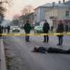 A somber urban street scene in Tula, Russia, early morning light, with police tape and a subtle indication of a tragic event: a faint outline of a woman lying on the pavement, surrounded by discreet police presence and a few onlookers, conveying a serious but respectful atmosphere without graphic detail