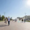 A bright sunny day in Saransk with people in light clothing walking on a street, heat waves rising from the pavement, a clear blue sky, no text or numbers