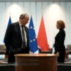 A dignified diplomatic scene showing a former Russian prime minister standing beside a suggested candidate for dialogue, both in formal attire, with a round table between them. In the background, subtle silhouettes of the European Union flag and the Russian flag overlap, symbolizing cooperation. The setting is a modern conference room with soft lighting, emphasizing a hopeful and constructive atmosphere.