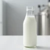 A high-quality photorealistic image of fresh milk in a clean glass bottle placed on a white surface, with a subtle background hint of a modern dairy processing facility, emphasizing purity and safety, with soft natural lighting highlighting the milk's smooth texture