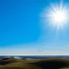 A peaceful, sunlit landscape of the Volgograd region on a clear day, showing rolling steppe, the Volga River, and distant city silhouettes under a bright blue sky; faint, soft aurora-like magnetic field lines subtly visible in the upper atmosphere to suggest calm geomagnetic conditions, with no storm clouds or threatening weather elements