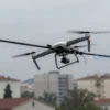 A realistic depiction of a drone wreckage partially collapsed on overhead power lines in Sevastopol, with visible broken wires, sparks, and a city skyline in the background, showing the damage caused by the debris.