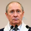 A realistic portrait of a middle‑aged Russian male diplomat standing at a podium with a subtle Russian flag backdrop, looking serious and thoughtful, representing a news interview about the expected duration of the conflict