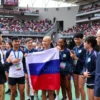 A vibrant international university sports competition scene showing diverse athletes in action, with a group of Russian athletes prominently participating and receiving a warm welcome from officials, set in a modern stadium filled with cheering crowds and colorful flags, emphasizing unity and sportsmanship