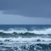 A dramatic seascape showing a stormy North Atlantic scene with dark, heavy rain clouds covering the sky, intense rain falling onto rough, choppy ocean waves, and a faint horizon line under overcast conditions, conveying the sense of strong localized rain in the NAO region