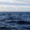A calm North Atlantic Ocean scene under a partly cloudy sky, with gentle waves and a soft sunrise glow indicating a mild temperature of around 5 degrees Celsius, without any text, numbers, or human-made structures.
