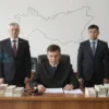 A solemn Russian courtroom scene in Dagestan, with a judge seated at a wooden bench, a gavel, and several men in business attire standing before the judge. On the table lie stacks of cash bundles and legal documents, but no visible text or numbers. In the background, a subtle outline of the map of Dagestan is visible on a wall, rendered abstractly without letters. The atmosphere is serious and authoritative.