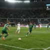 A dynamic football match scene between FC Sochi and Zenit in the Russian Premier League, featuring players in action on a lush green pitch, a stadium filled with cheering fans, bright stadium lights, and a neutral scoreboard indicating a draw, all depicted without any text or numbers