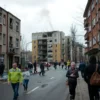 A realistic scene of an urban street in Volgograd after a drone attack, showing a partially damaged residential building with broken windows and smoke rising, emergency responders guiding civilians out of the building, families carrying belongings, and a sense of organized evacuation, under a cloudy sky, without any visible weapons or graphic gore.