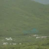 A bright sunny landscape of the Komi region with clear blue sky, green forests, rolling hills, and a small village in the distance, capturing the warm +20°C weather on May 21.