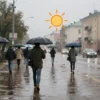 A rainy street scene in Saransk on a warm day, showing wet pavement, umbrellas, a cityscape, and a subtle weather icon indicating warmth