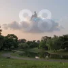 A serene park at sunset with lush trees, winding paths, and a gentle pond reflecting soft light. Musical notes drift like fireflies above the grass, evoking a melody. In the sky, a fluffy white cloud carries a subtle silhouette of a figure watching the park below, their posture relaxed and contemplative. Two overlapping translucent circles subtly form the shape of the number 88 within the clouds, integrated naturally without obvious text. The scene is peaceful, dreamy, and slightly magical.