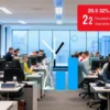 A modern office scene showing a group of diverse employees working at desks, with a large transparent clock overlay indicating time, and a visual representation of a doubled overtime limit such as two stacked hourglass shapes or a bar graph rising, all in a bright, professional atmosphere