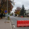 A quiet urban street in Voronezh with a red roadblock and a universal no‑entry symbol, empty sidewalks, autumn trees lining the road, and a cloudy sky overhead