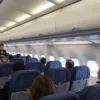 An interior view of a commercial airplane cabin on flight J2021 of AZAL heading to Israel, showing passengers seated, flight attendants, overhead bins, and the plane's windows with a view of clouds and a hint of the Israeli landscape below, all in a realistic style.