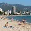A realistic panoramic view of Sochi's Black Sea coastline with the Caucasus mountains in the background, a sunny beach with families and tourists enjoying, and a subtle hint of a ranking chart overlay in the corner