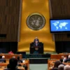 A diplomatic scene inside the United Nations General Assembly hall, showing a Chinese delegate standing at a podium delivering a speech, with a subtle backdrop of the Ukrainian flag and a world map, capturing a serious and somber atmosphere. The audience includes delegates from various countries, and the lighting emphasizes the gravity of the discussion without any visible text or signage.
