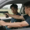 A teenage boy inside a P-3 vehicle pulling a handgun and pointing it at another teenage boy, with a tense, dramatic atmosphere, no graphic violence or gore, no text or lettering