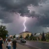A dramatic storm scene over the city of Astrakhan on May 18, featuring dark storm clouds, lightning, strong wind blowing through the streets, and residents looking up or seeking shelter, with no text or signage visible
