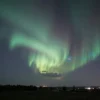 A dramatic evening sky over the Rostov region with swirling magnetic storm auroras, illuminated clouds, and a distant city silhouette, with subtle hints of the region's landscape