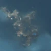 A realistic satellite in low Earth orbit above the ocean, its sensor array pointing downward, with a detailed map of the sea surface below showing clusters of floating debris detected by the satellite. The scene should emphasize the contrast between the clear blue water and the scattered trash, highlighting the satellite’s role in monitoring ocean cleanliness.