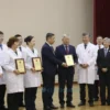 A group of 50 healthcare workers in Chelyabinsk Oblast are receiving awards from the governor. The scene takes place in a formal setting, possibly a hall or auditorium, with a stage and podium. The governor is handing out certificates or awards to the medical professionals. The atmosphere is celebratory and respectful. Focus on the people and the act of awarding.