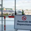 A temporary sign or barrier at Volgograd Airport indicating a restriction on receiving and dispatching flights, with airport infrastructure and aircraft visible in the background, showing a controlled environment with staff monitoring operations
