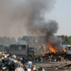 A wide shot of a landfill in Rostov Veliky, Russia, possibly on fire. The scene should depict piles of garbage, smoke rising into the sky, and potentially flames visible. The overall atmosphere should be one of environmental concern and potential danger.